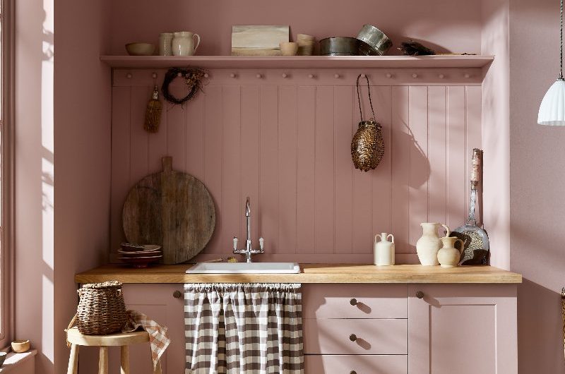 A pink utility with painted units, wood worktop, matching pink panelling and open shelf, with a sink and sink skirt, and wood flooring.