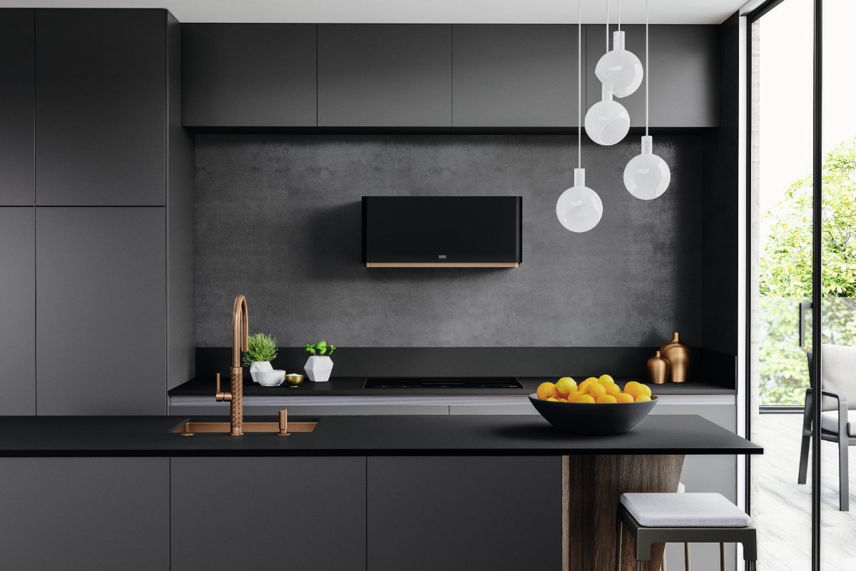 A matt black kitchen with handleless cabinetry, dark work surfaces, a copper sink and tap, and a statement extractor.