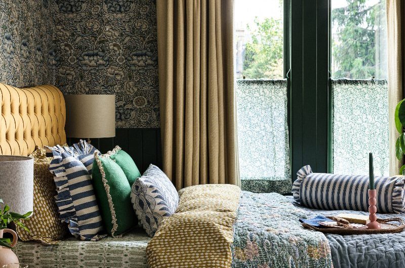 A bold bedroom design with layered patterned bed linen, cushions, and throws in mustard yellow, deep green and dark blue shades.