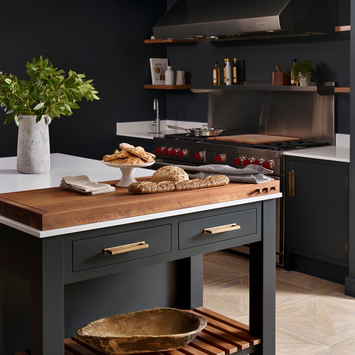 A dark kitchen design with sleek cabinetry, a freestanding island with a chopping block and industrial appliances.