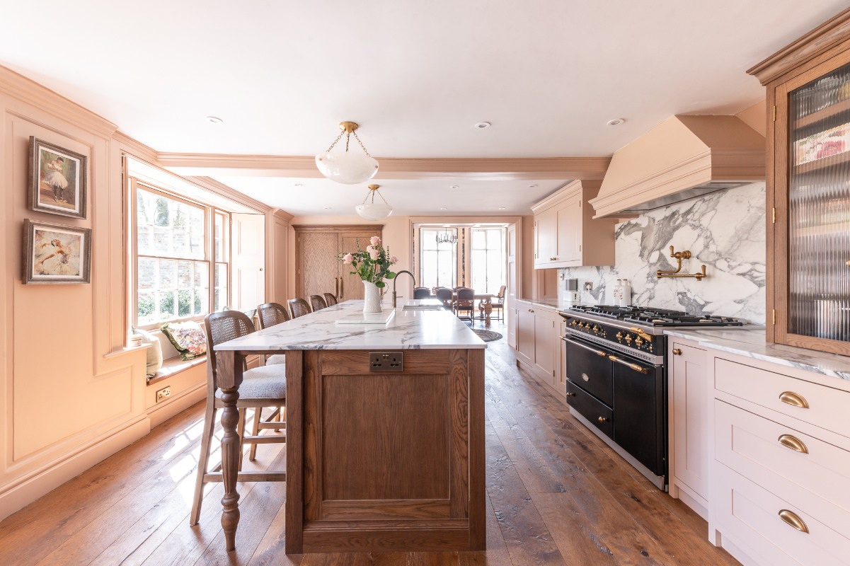 A pale pink kitchen with statement marble and an oak island, filled with light through French windows in the dining room.