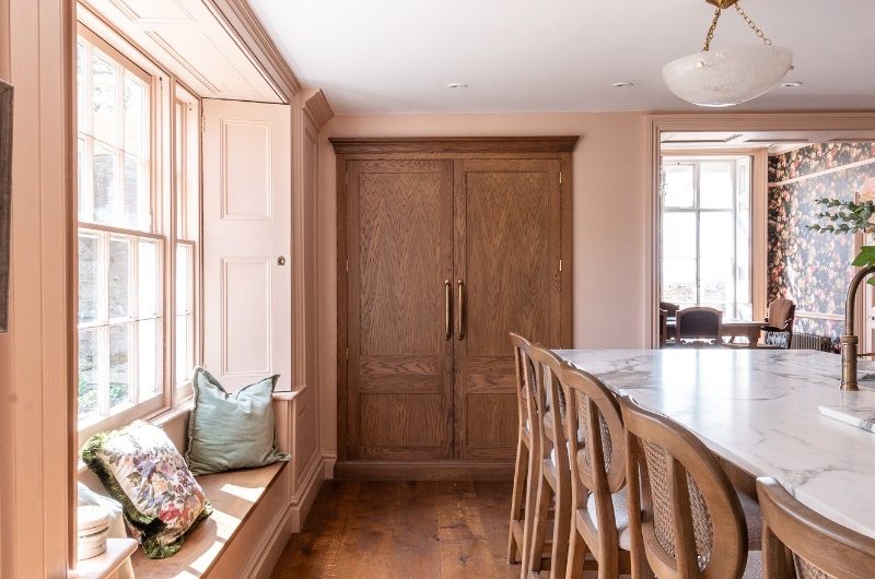 View of the kitchen island with six bar stools, a double door pantry, and a window seat.