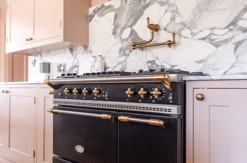 A cooking area with a black range cooker, veined marble, a pot filler tap, and a bespoke overmantel.