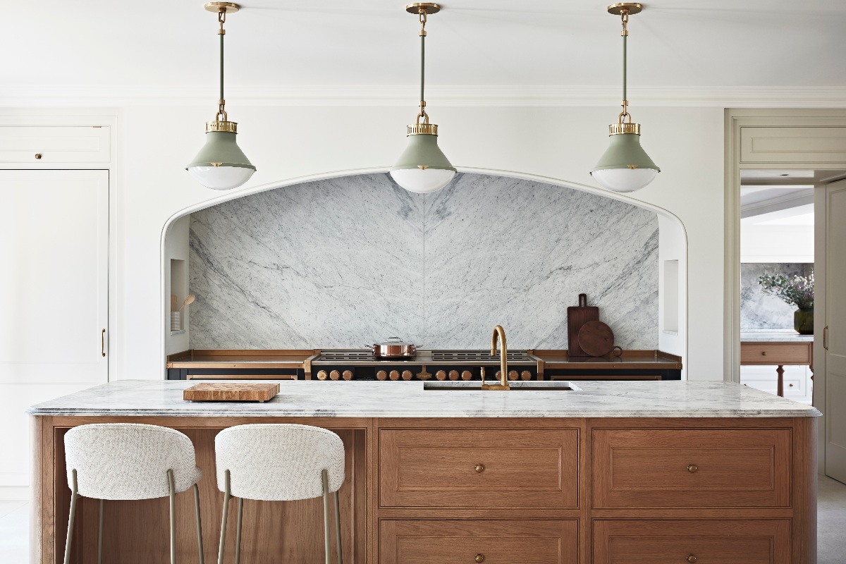 A fusion kitchen with a statement cooking zone with an arched alcove, range cooker, bookmatched surfaces, and a central island with a wood base and elegant worktop.