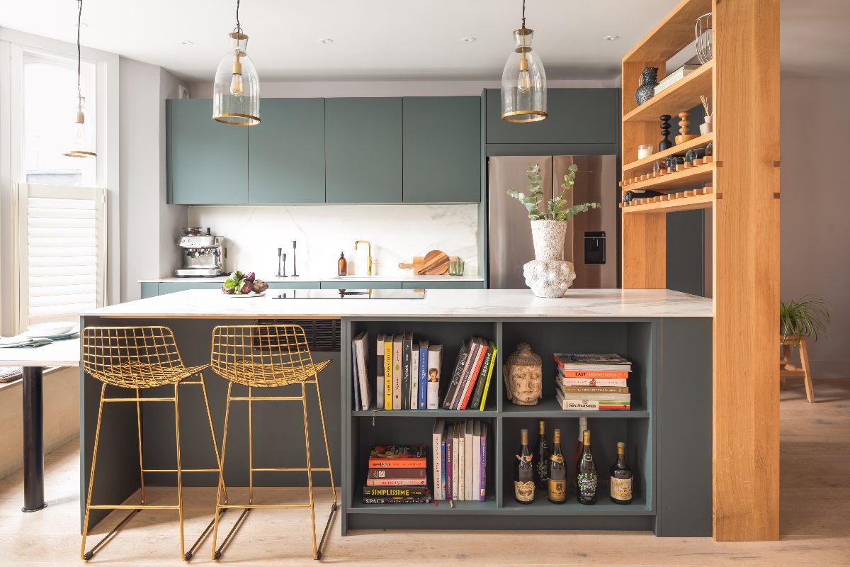 A modern kitchen design with handleless green cabinets, an island with seating and storage, plus a wood shelf area which also helps zone the space.