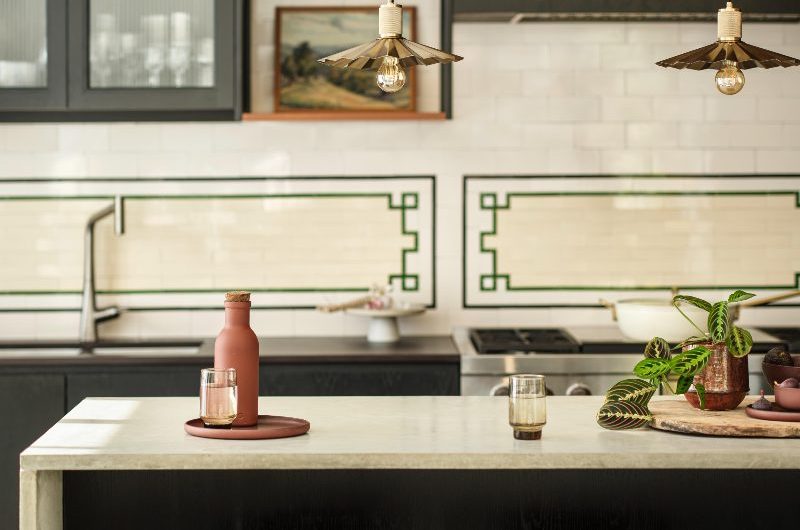 A statement dark kitchen with metro wall tiles, an intricate splashback, a central island, dark units, and industrial lighting.