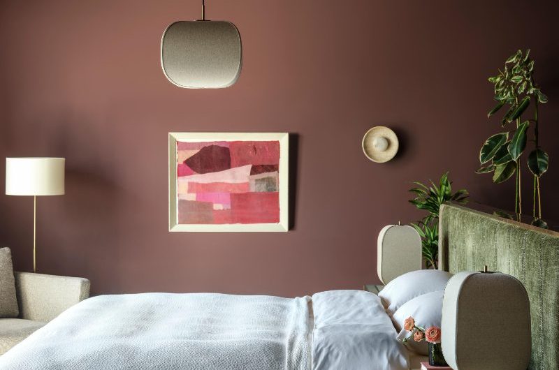 A boutique bedroom with green bed frame, layered lighting, and moody wall paint.
