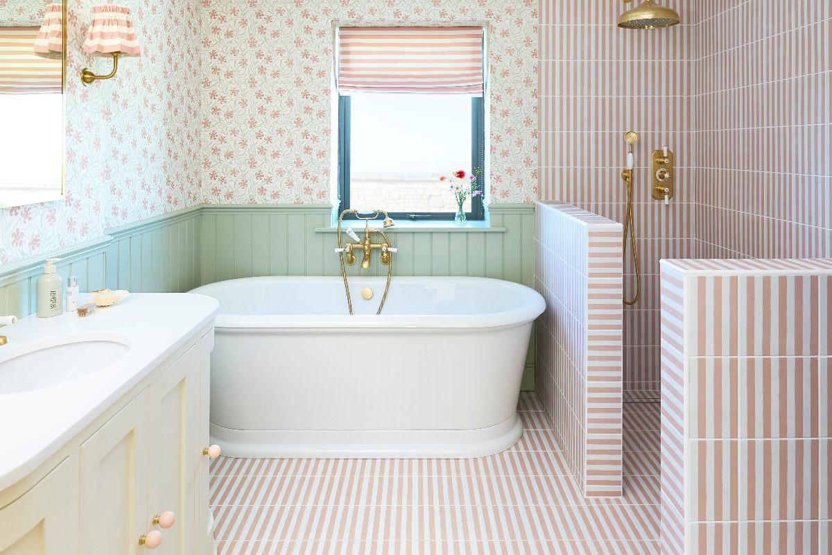 A playful wetroom with striped tiles, floral wallpaper, sage green panelling, an open shower, a freestanding tub, and a Shaker vanity.