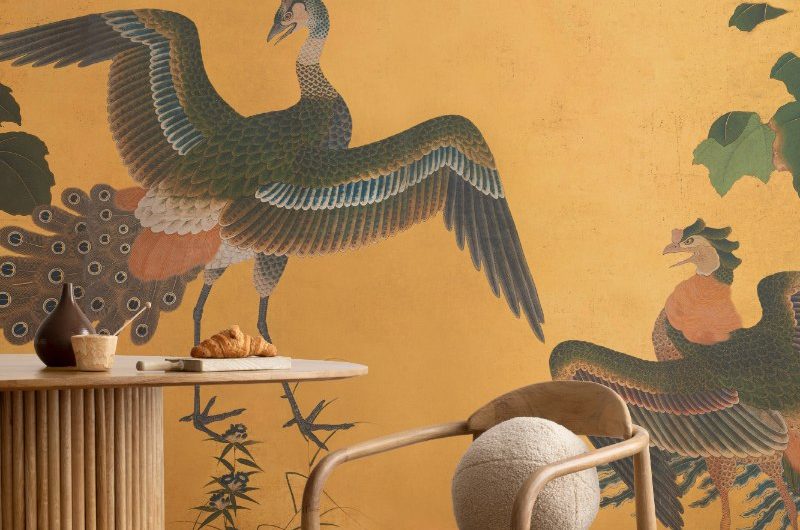 A living room with a yellow mural with wood flooring and wood table and chair set.