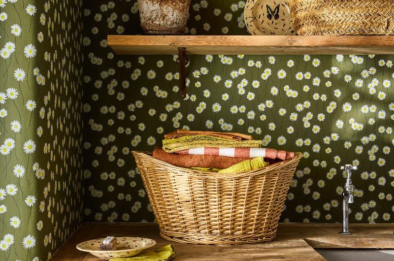 A country chic utility room with dainty daisy patterned wallpaper on a dark olive green background with wood furniture and shelving.