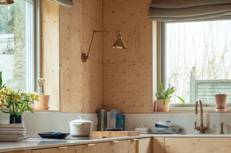 A kitchen design with blonde wood cabinetry, white worktops, wood wall and ceiling cladding, and brass accents.