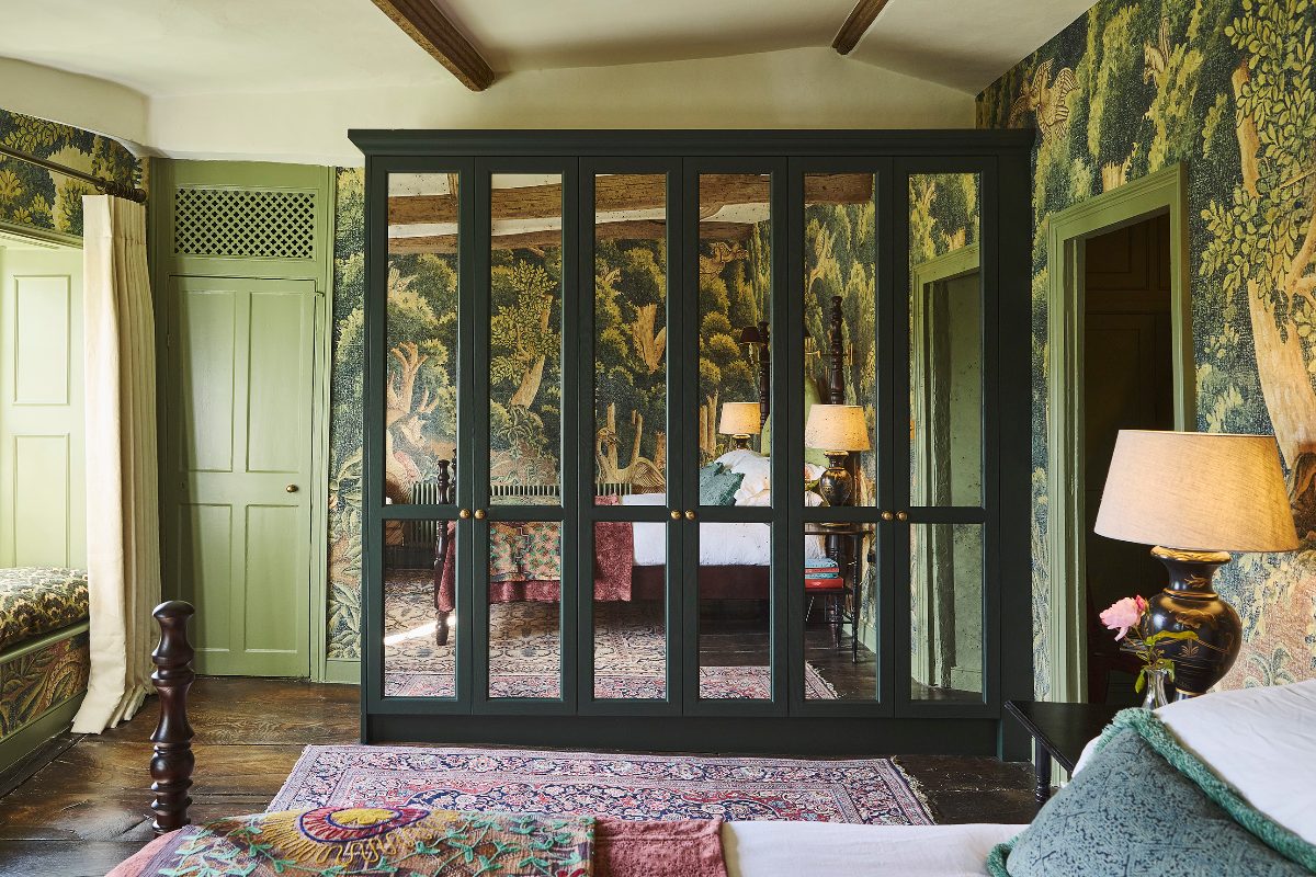 A biophilic bedroom design with nature-inspired wallpaper, bespoke green wardrobes with mirrors, and colourful furnishings.