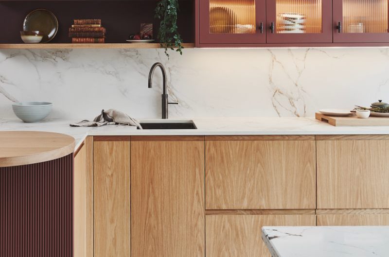 A modern scheme with wood cabinets, burgundy wall units with reeded glass and wood open shelving.