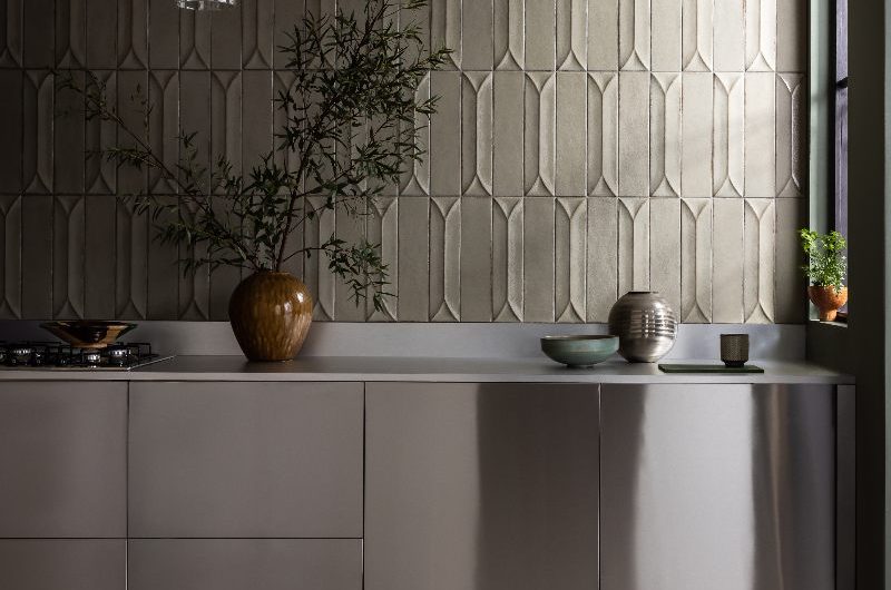 Modern kitchen zone with stainless steel units, 3D wall tiles, stone flooring and minimalist decor.