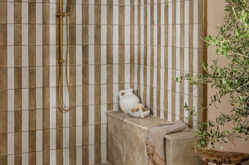 A spa-like bathroom with a striped shower, gold shower system, a stone clad shower seat and stone flooring.