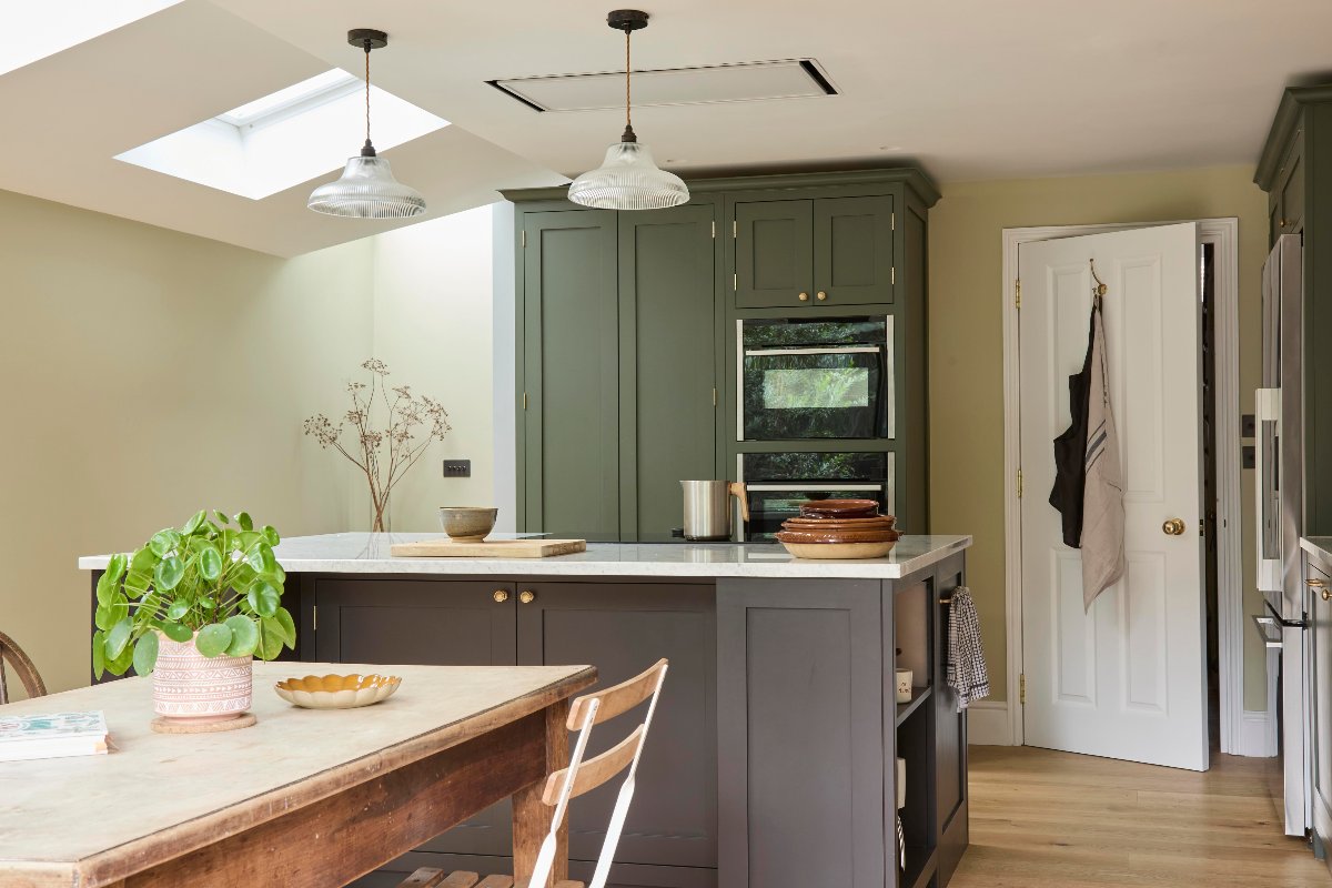 A classic Shaker kitchen with tall green units, a brown island, and an adjoining dining area.