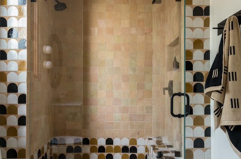 A bathroom design with a shower room clad in zellige tiles, ceiling included, with a glass panel and black fittings.