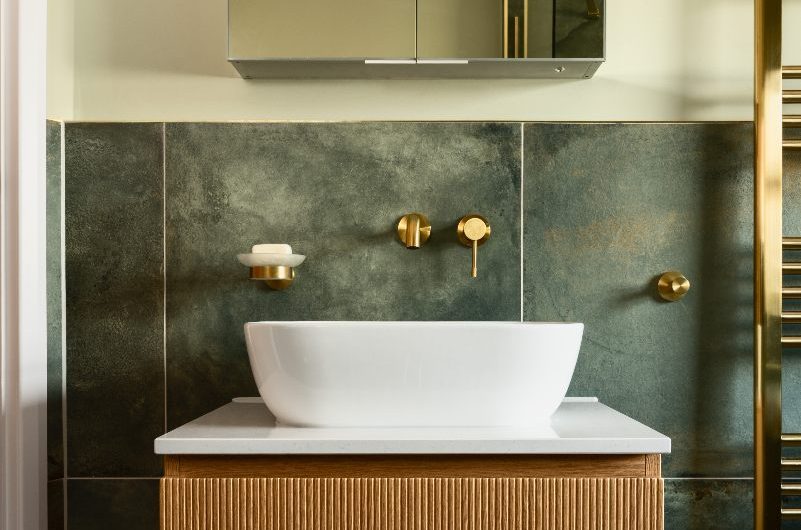A wall-mounted vanity unit with a fluted wood finish, sleek white countertop basin, brass tap, and a mirror cabinet above it.