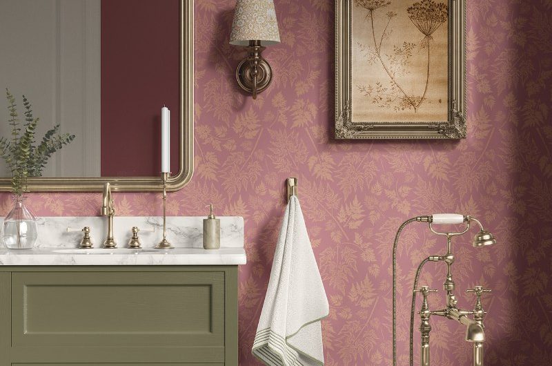 A bathroom design with pink nature-inspired wallpaper, a green vanity, a freestanding tub, and classic fittings.