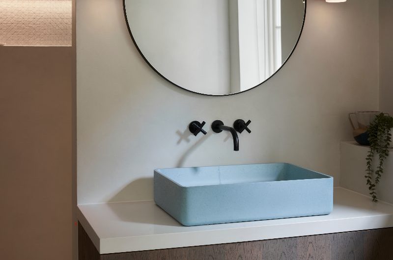 Calm bathroom vanity zone with a wood vanity, blue basin, black brassware, and layered lighting.