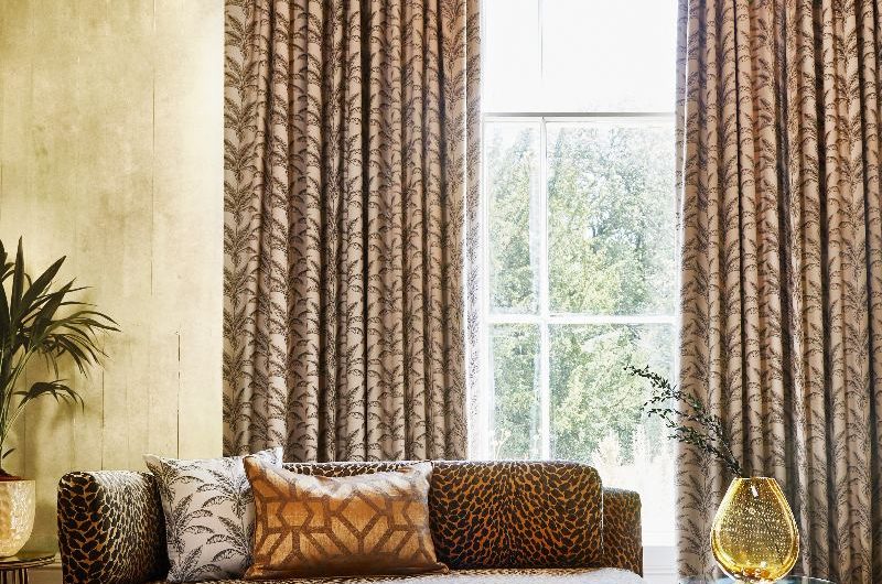 A living room with animal print sofa and patterned cushions and curtains on tall windows.