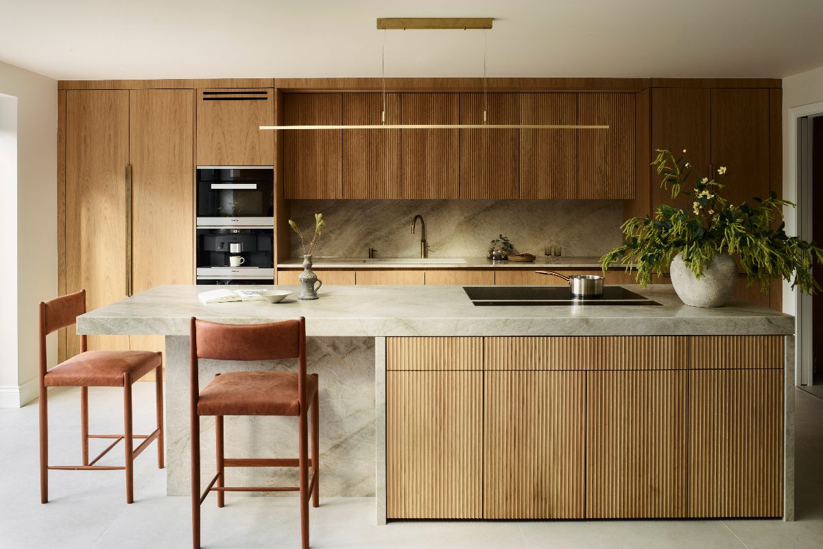 Nature-inspired kitchen design with fluted wood and grainy wood cabinets, a stone and fluted wood island with a hob and seating, and metallic lighting and brassware.