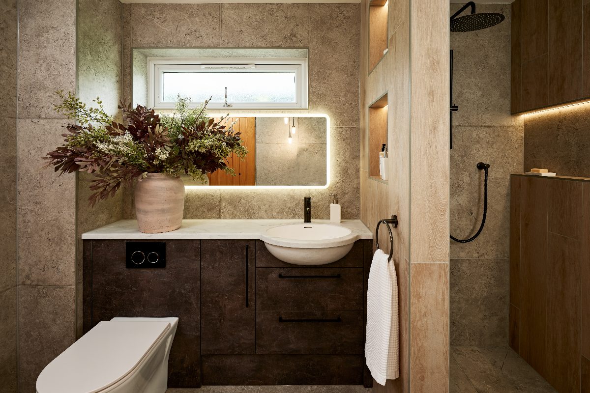 A modern bathroom with stone-effect wall and floor tiles, with a stud wall separating the shower from the vanity area.
