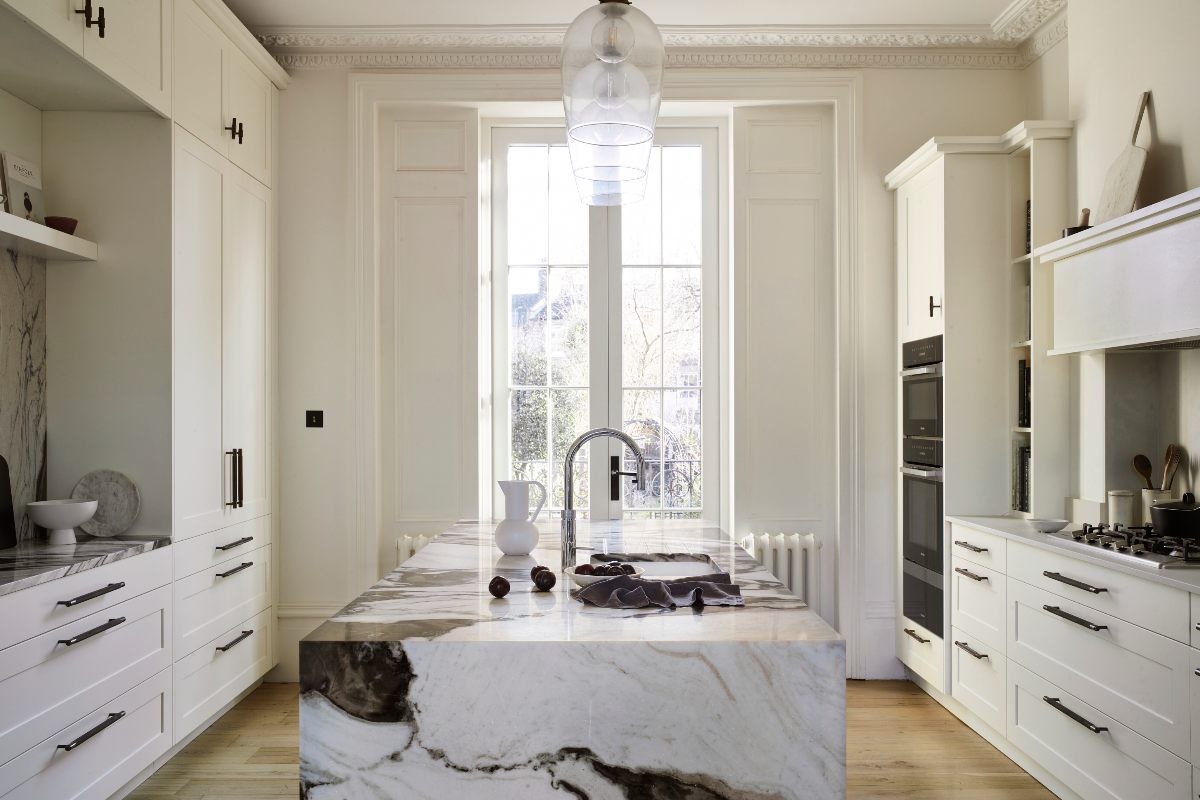 A double galley layout with a centrals stone-clad island with a tall window and white furniture.