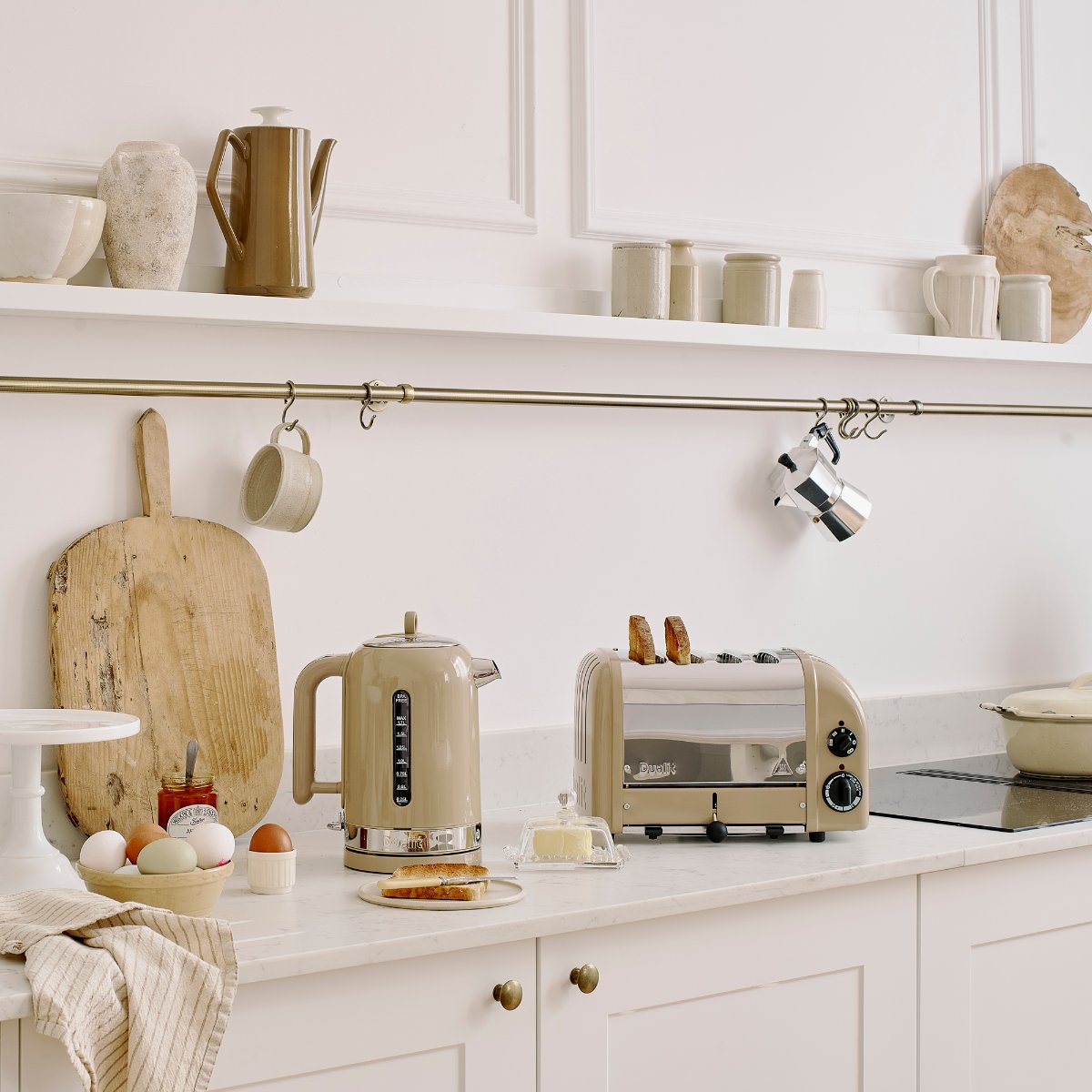 A classic Shaker kitchen with elegant countertops, open shelving, a brass rail, and a neutral kettle and matching toaster.