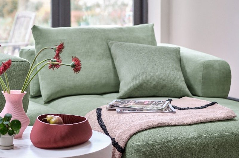 A living room with a green love seat, checkered rug, and quirky side table.