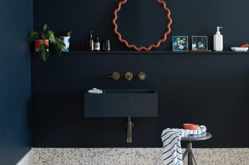 A navy bathroom with dark walls and matching concrete basin, and white speckled flooring.