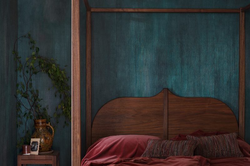 A dark bedroom design with blue ombre wallpaper and a four poster wooden bed.