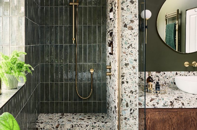 A walk-in shower with green metro tiles, a terrazzo shower seat, and a gold shower system.