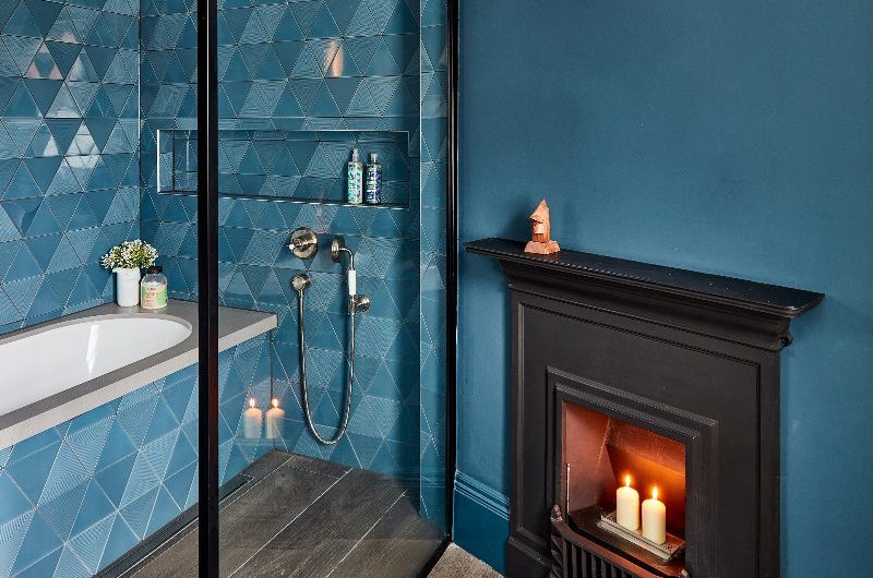 A blue bathroom design with blue wall paint, blue tiles, a fitted tub, separated by a glass screen.