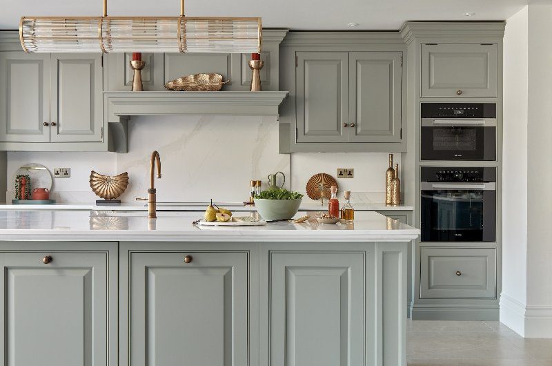 A classic kitchen in sage green with a central island, stone flooring, and warm brass accents.