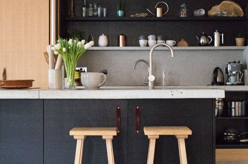 A modern scheme with dark wood units, concrete-effect worktops, chrome tapware, open shelving, and statement lighting.