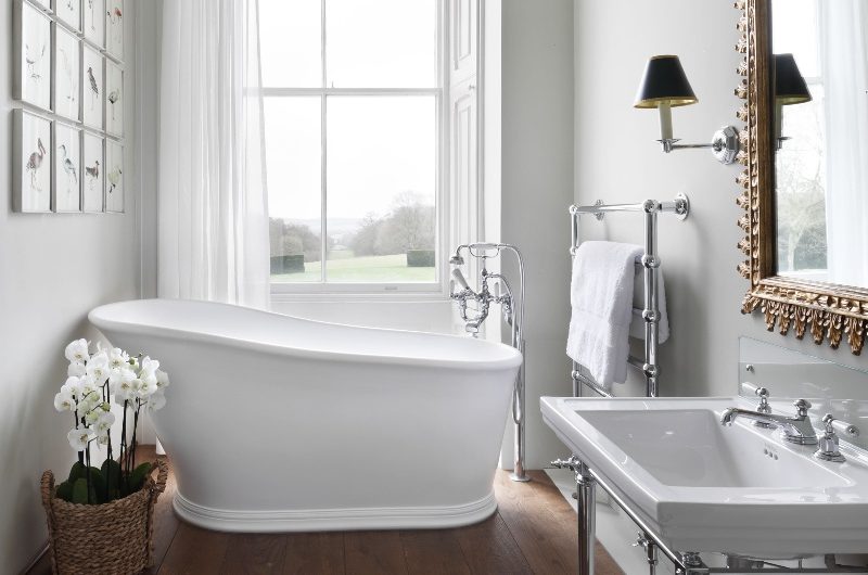 A classic bathroom with a pedestal vanity unit, a split-level wood floor and slipper bath by the window.