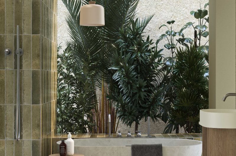 A spa bathroom with tall greenery, green tiles, a freestanding tub, and terrazzo flooring.