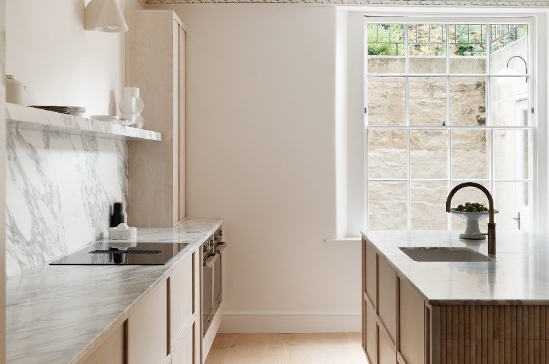 The layout of the minimalist kitchen with a run of cabinets which offers storage and the cooking zone and a statement island with a built-in sink and tap.