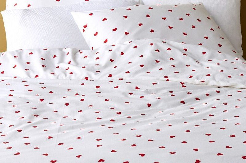 A neutral bedroom interior with white and red heart bedding.