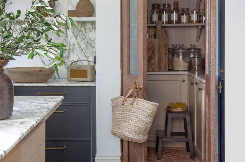 A classic kitchen design with dark cabinetry, a small walk-in pantry with curved entrance, neutral cabinets, terracotta flooring, and open shelving for storage jars.