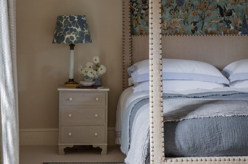 A simple sleep space with a four poster bed, light wood furniture and a natural rug with a blue border rug.
