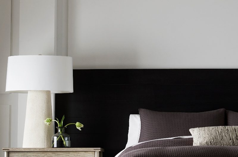 A sleep space with an extra long headboard, a large side table and oversized lamp.