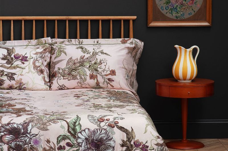 A moody bedroom design with wood flooring, an abstract rug, low wood bed with floral bed linen, and dark painted walls.