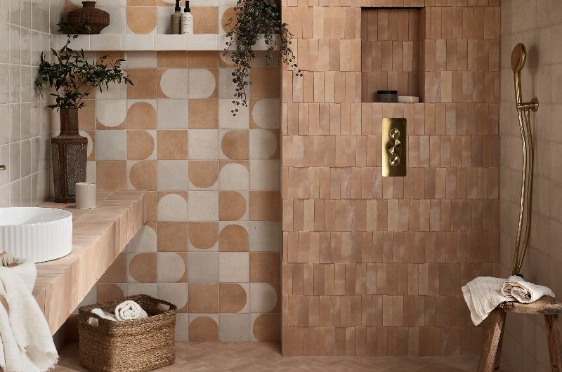 A neutral bathroom layered in texture with metro and patterned tiles in earthy hues, with gold brassware, and tactile flooring.