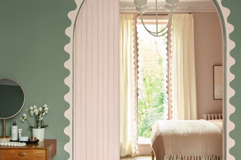A colourful bedroom design with green walls and a pink scalloped border and matching sliding door, with herringbone wood flooring and minimalist furniture.