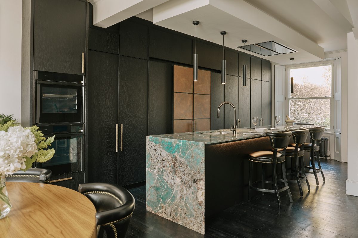 A dark and metallic design with floor-to-ceiling cabinetry, colourful stone-clad island with seating, and integrated appliances.