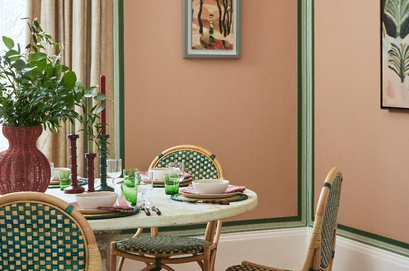 A dining room with pale pink walls and green architraves, with colourful chairs and a tactile dining table.