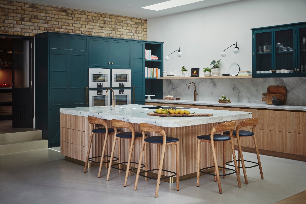 A modern teal and wood kitchen with a hidden pantry and a central multi-functional island with a fluted base, seating, a sink and tap, hob, and chunky marble worktop.