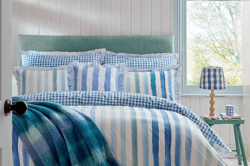 A sunny sleep space with pops of blue, from the striped bedding, teal headboard, teal side table, and blue lighting and decor.